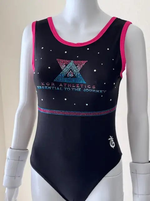 Black sleeveless gymnastics leotard with pink trim, a rhinestone-embellished triangular logo and text reading ’kcr athletics essential to the gymnast,’ and a small white embroidered emblem on the lower