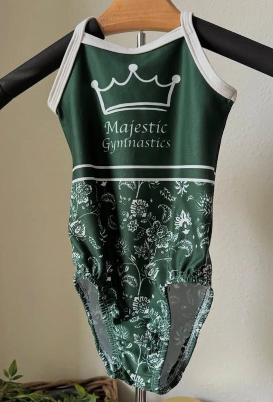 A dark green gymnastics leotard with white trim, a crown logo and ’majestic gymnastics’ text above an intricate floral pattern.