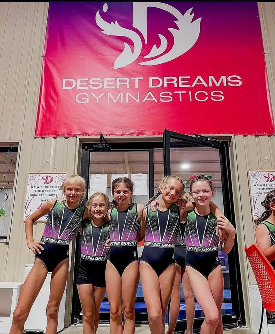 The girls are wearing matching black and gradient purple-to-pink leotards with ’fleeting gravity’ printed across the chest.