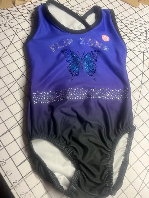 A vibrant royal blue and navy gradient gymnastics leotard featuring a sparkling butterfly design adorned with rhinestones across the chest, accented by a horizontal band of shimmering crystals.
